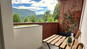 A balcony with a wooden table, two wooden chairs, a cushioned stool, and a potted plant.
