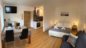 A modern apartment with a dining area, kitchenette, and a bedroom with a bed and nightstands.