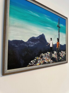 A framed painting of a mountain landscape with two figures, one standing and one sitting, against a backdrop of a cross and a clear sky. - Bijol Apartments - 1-bedroom Apartment K (Bled)