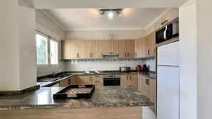 A modern kitchen with wooden cabinets, a granite countertop, a built-in oven, and a refrigerator. - Three Bedroom Villa With Private Pool in Moraira (Teulada)