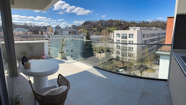 A balcony with a table and chair, a glass railing, and a view of buildings and trees. - Skyline Penthouse Retreat Luxury in Ljubljana (Ljubljana)