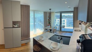 A modern kitchen with a central island, a dining area with a glass table, and a view of a building through large windows. - Skyline Penthouse Retreat Luxury in Ljubljana (Ljubljana)
