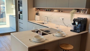 A modern kitchen with a central island, two stools, a coffee machine, and a window overlooking a balcony. - Skyline Penthouse Retreat Luxury in Ljubljana (Ljubljana)