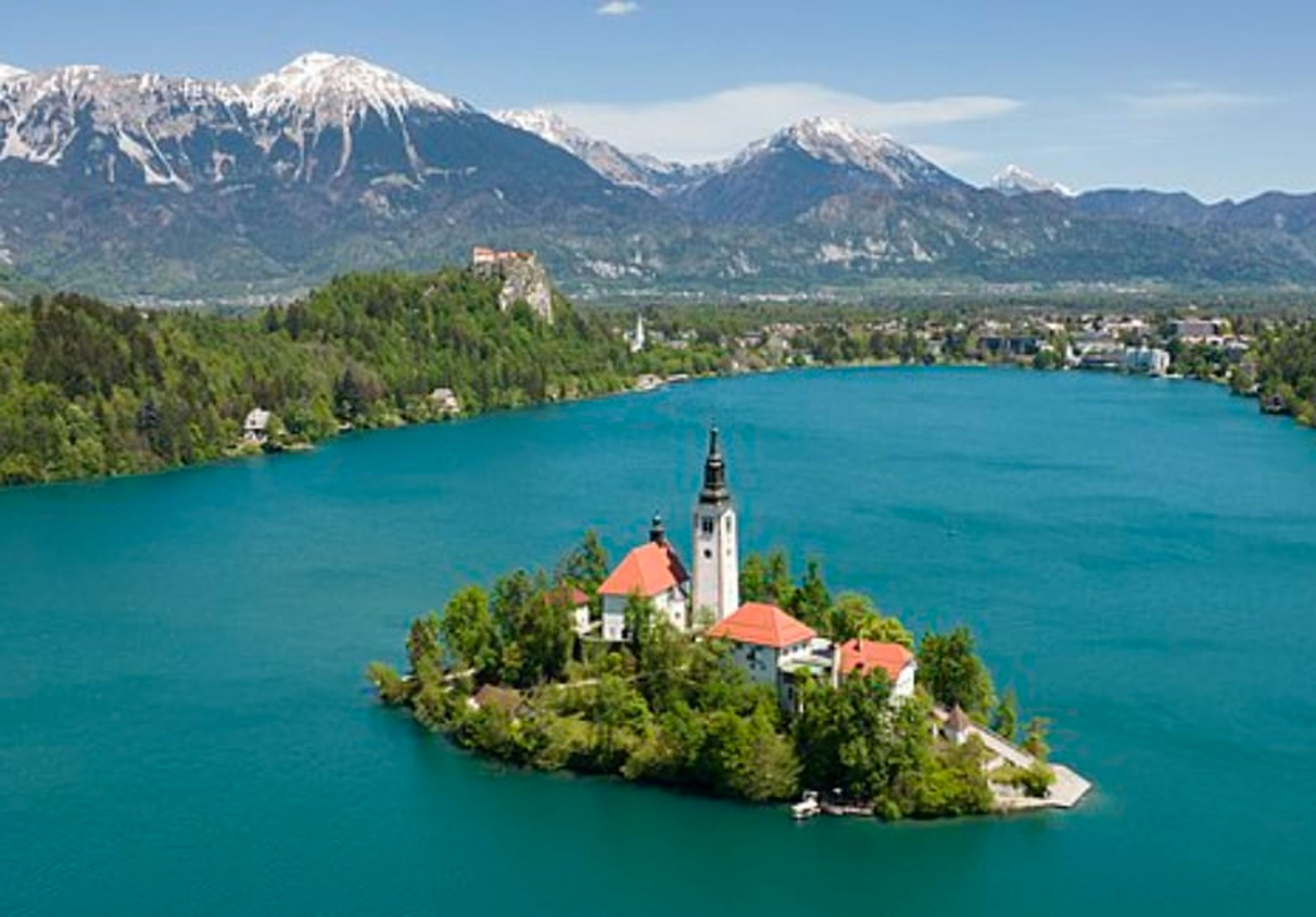 A church on a small island surrounded by a lake with mountains in the background.