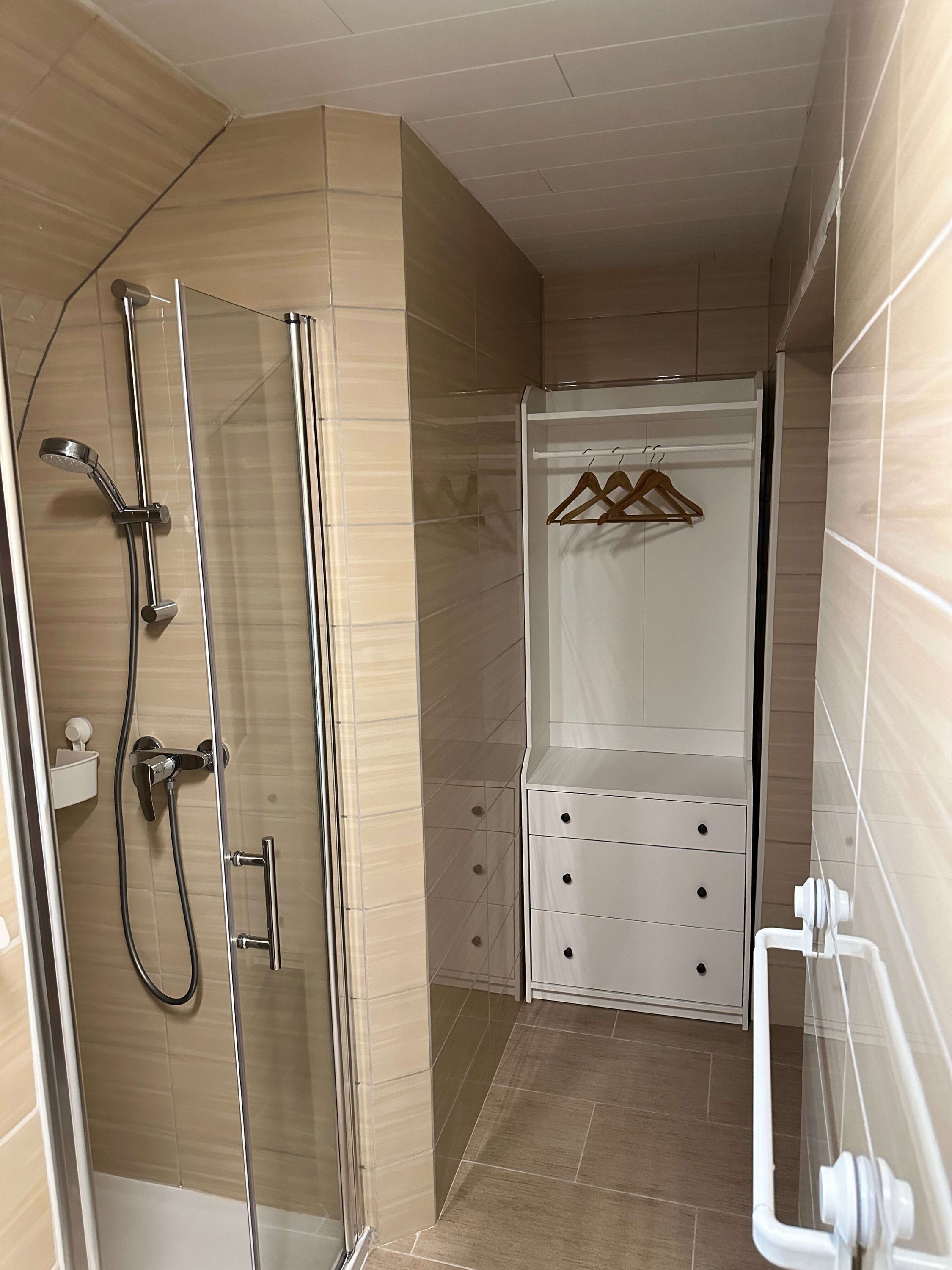 A bathroom with a glass-enclosed shower, a white cabinet with drawers, and a towel rack.
