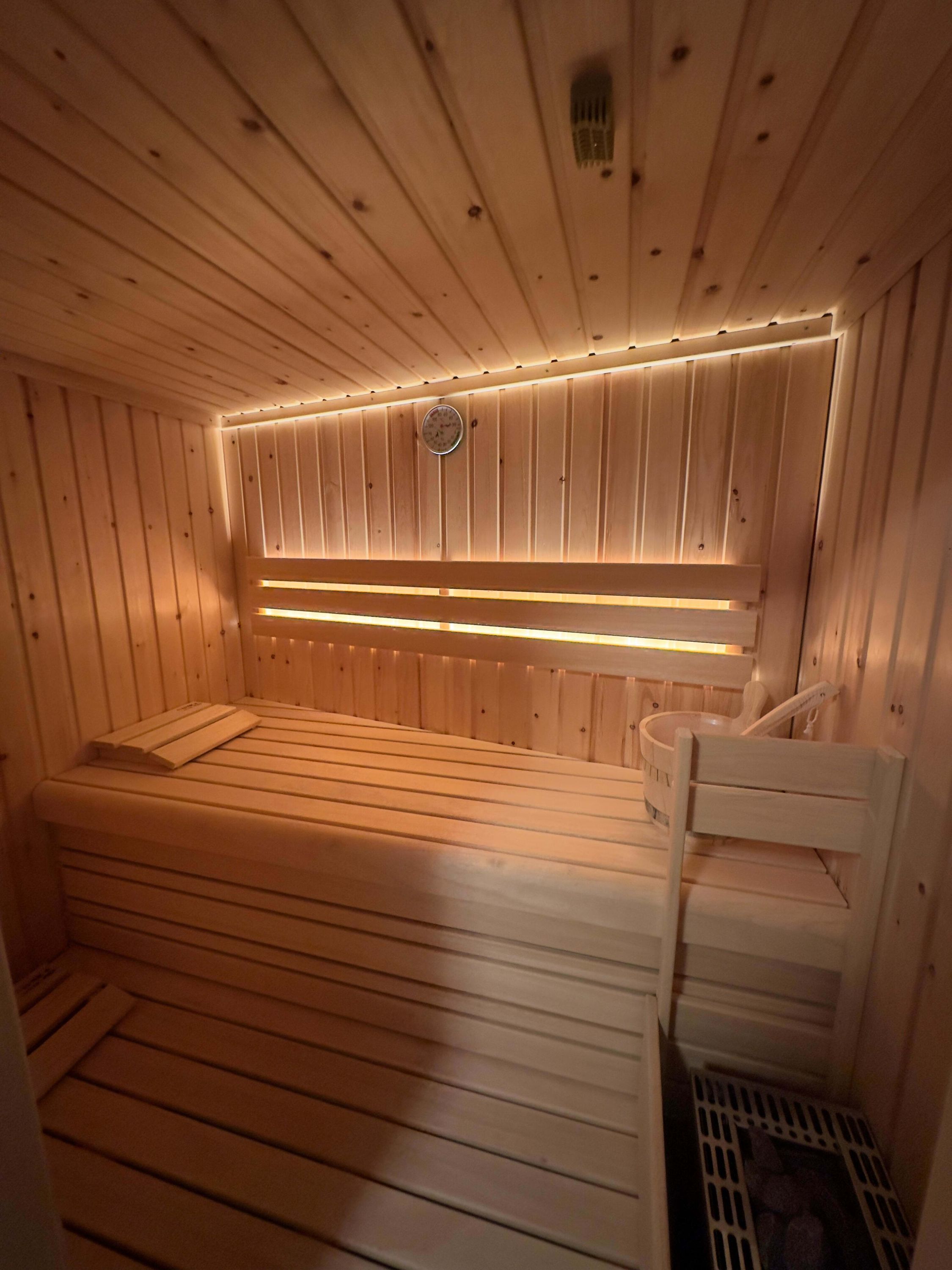 A sauna with wooden walls and benches, a visible heater, and a clock on the wall.