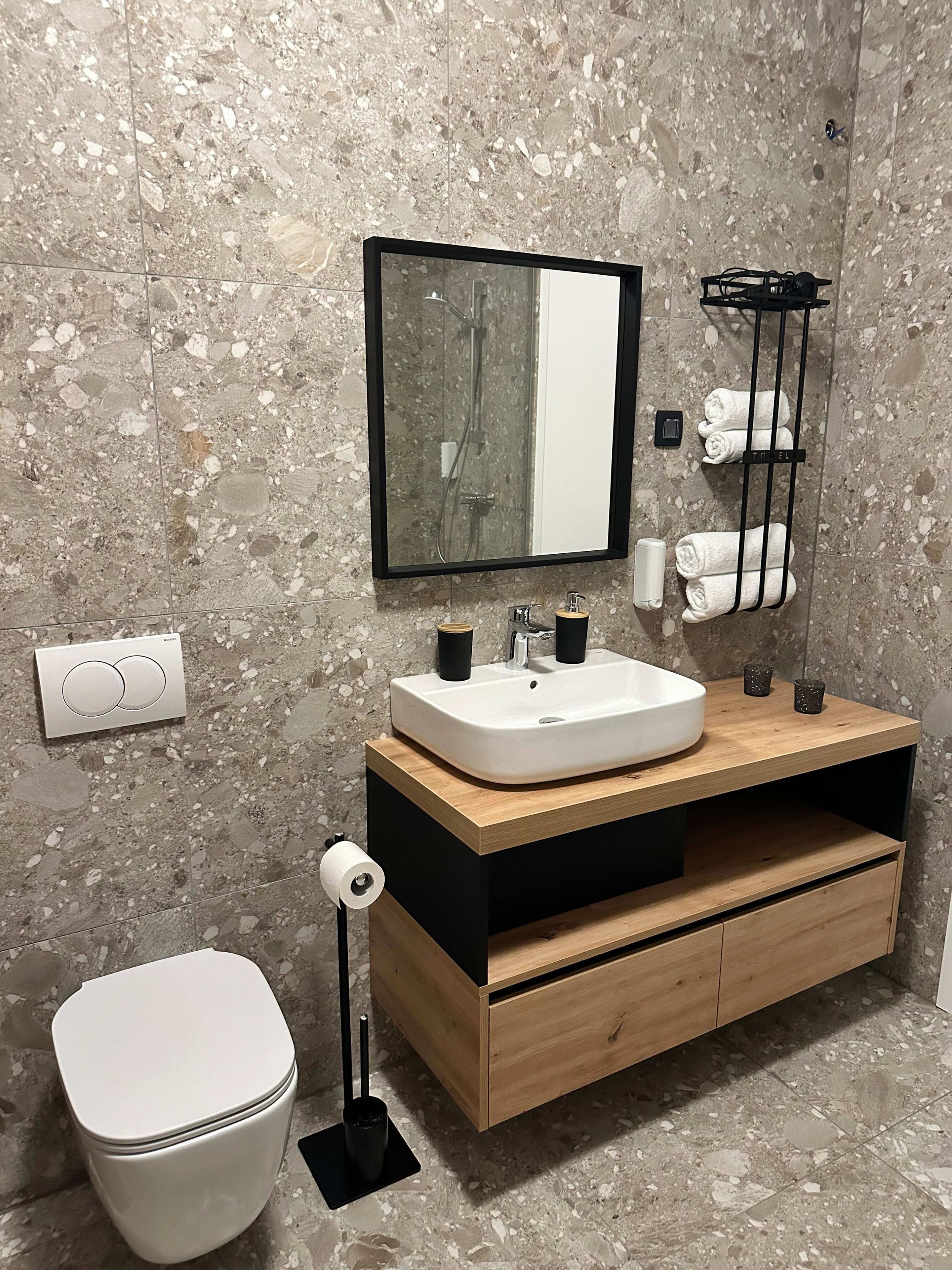 Un bagno moderno con un water bianco, un mobile bagno in legno con lavandino, uno specchio e un porta asciugamani.