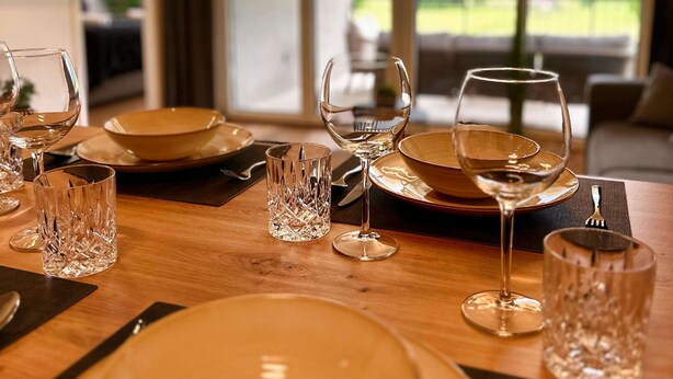 A dining table set with plates, glasses, and cutlery, with a view of mountains through large windows. - Soca Valley Suites - Premium Apartment A15 (Bovec)