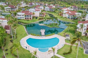 A resort with a central swimming pool, multiple buildings, and lush greenery. - Daria Beachfront Community Steps 2 Pool- Generator (Vega Alta)