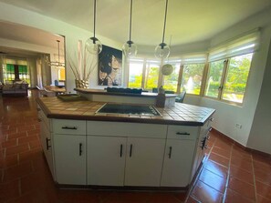 A spacious kitchen with a large island, white cabinets, and a view of greenery outside. - Daria Beachfront Community Steps 2 Pool- Generator (Vega Alta)