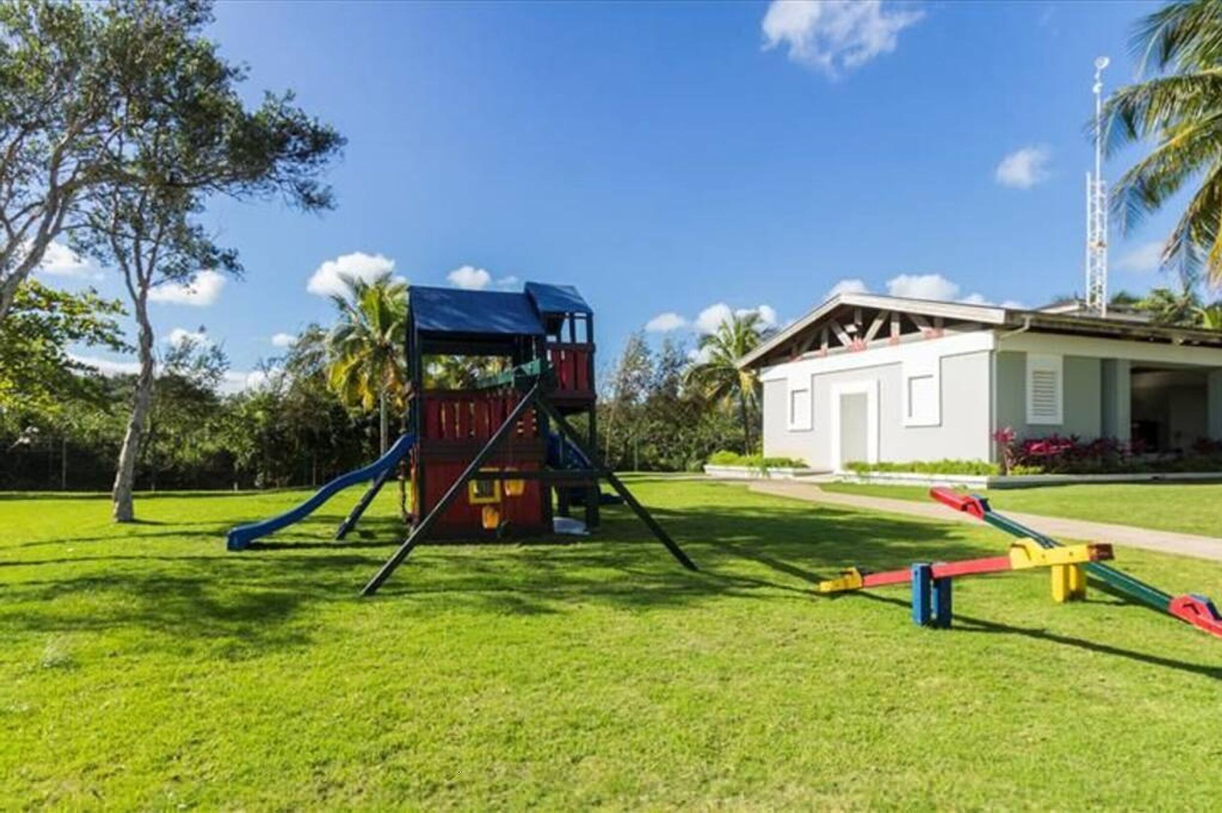 A playground with a slide and climbing structure, surrounded by a well-maintained lawn and a building with a white facade.