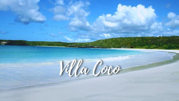 Une plage avec une eau d’un bleu limpide et une rive de sable blanc. On peut y voir l’inscription « Villa Coco ».