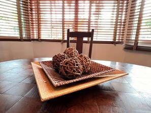 Una mesa redonda de madera con una cesta tejida que contiene objetos esféricos, un mantel individual tejido y una silla de madera.