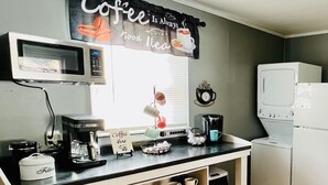 Ett kök med en kaffestation, en mikrovågsugn, en kaffebryggare och ett kylskåp.
