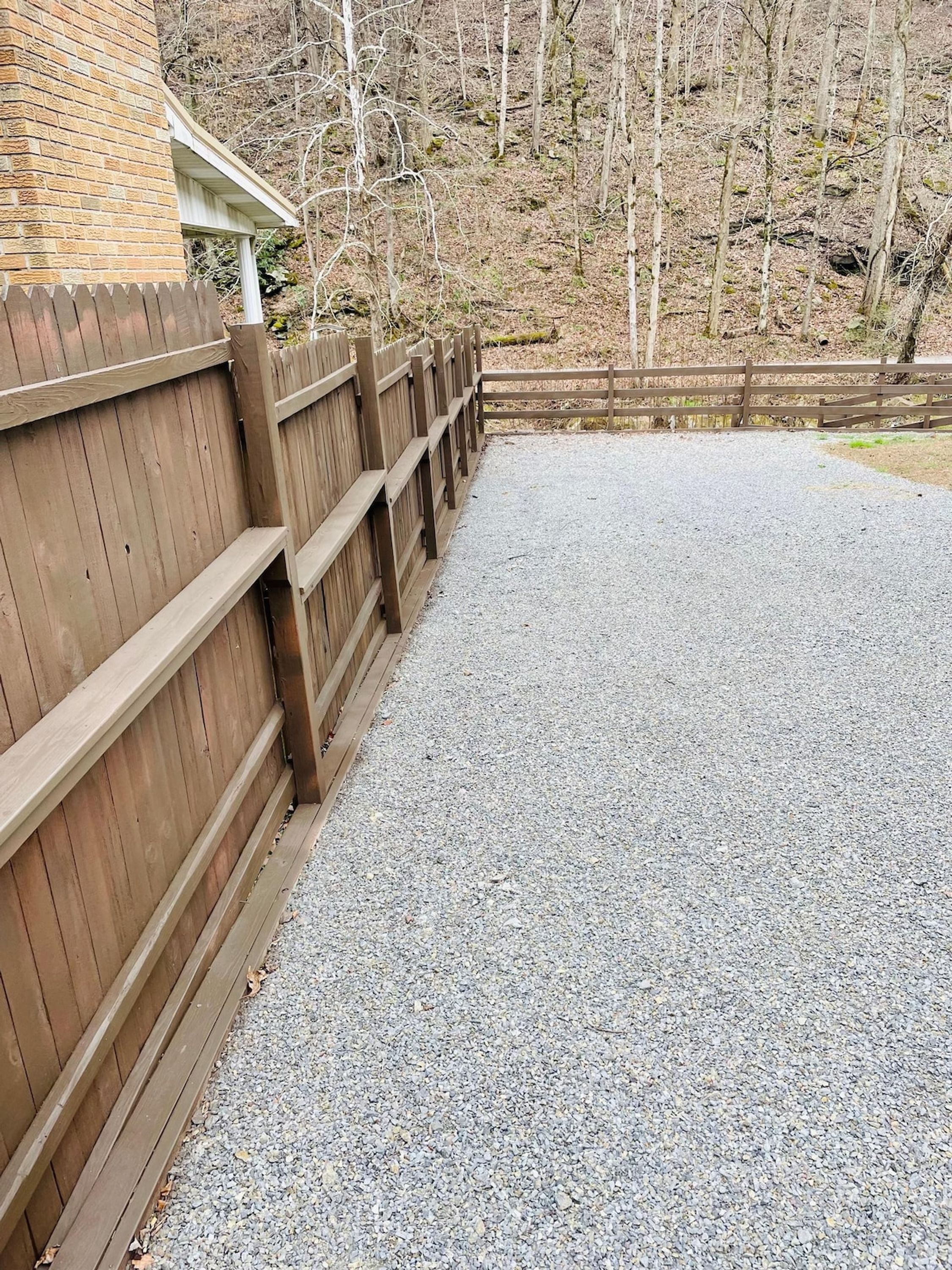 A gravel driveway leading to a wooden fence.
