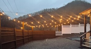 Un'area esterna recintata, illuminata da luci a catena, con pannelli in legno e una staccionata bianca.