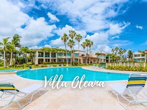 A resort with a swimming pool, palm trees, and a clear sky.