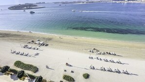 Une plage avec des transats et des parasols, une mer d’un bleu limpide et des bâtiments en arrière-plan.