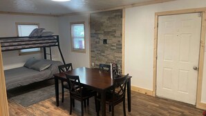 A room with a bunk bed, a dining table with chairs, a stone accent wall, and a door.