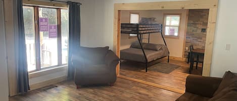 A living room with a brown sofa, a bunk bed, and a dining area with a table and chairs.