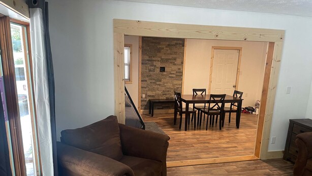A living room with a brown sofa, wooden flooring, a dining area with a table and chairs, and a stone wall.