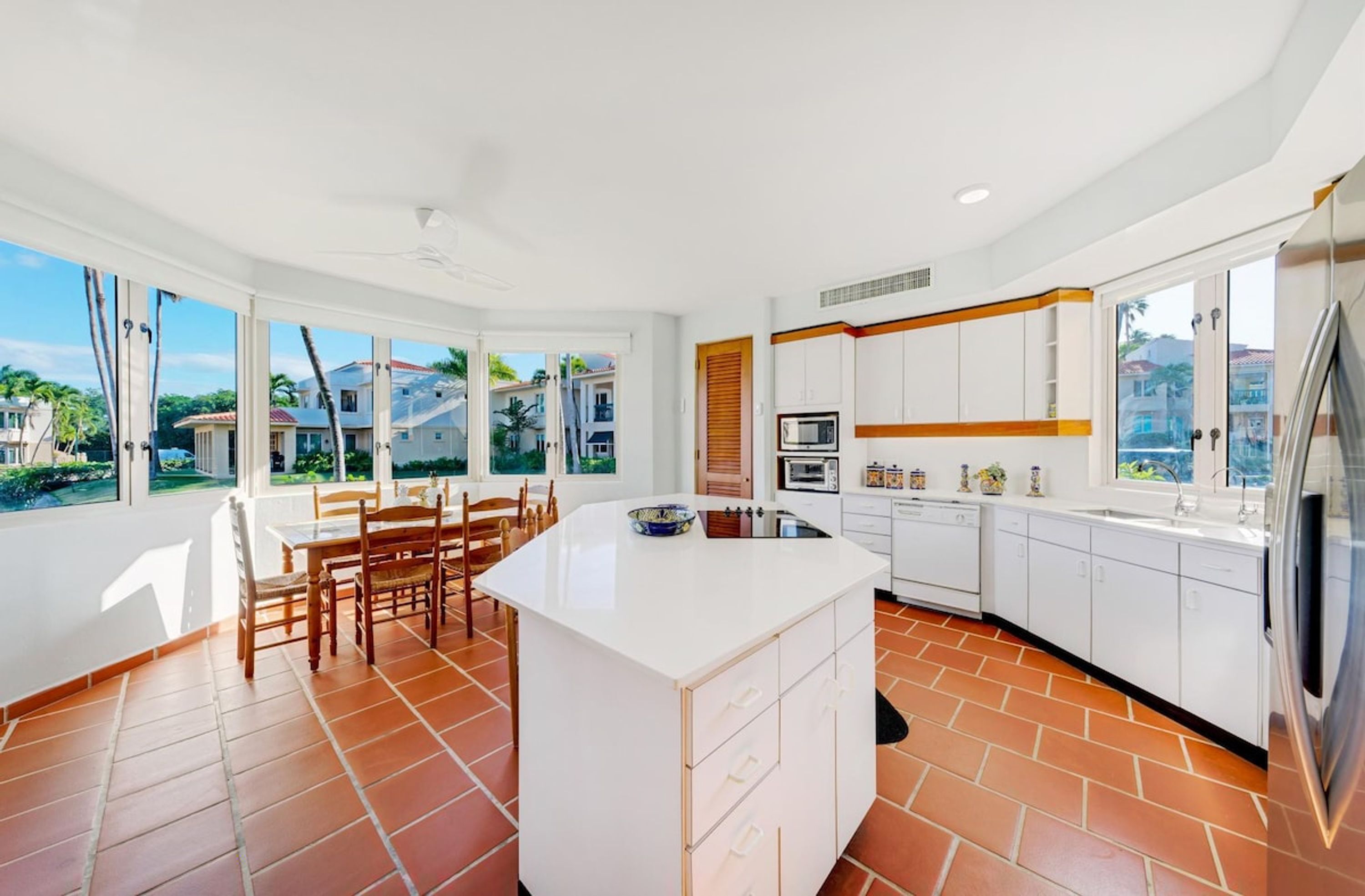 A modern kitchen with white cabinets, a central island, and a dining area with wooden chairs.