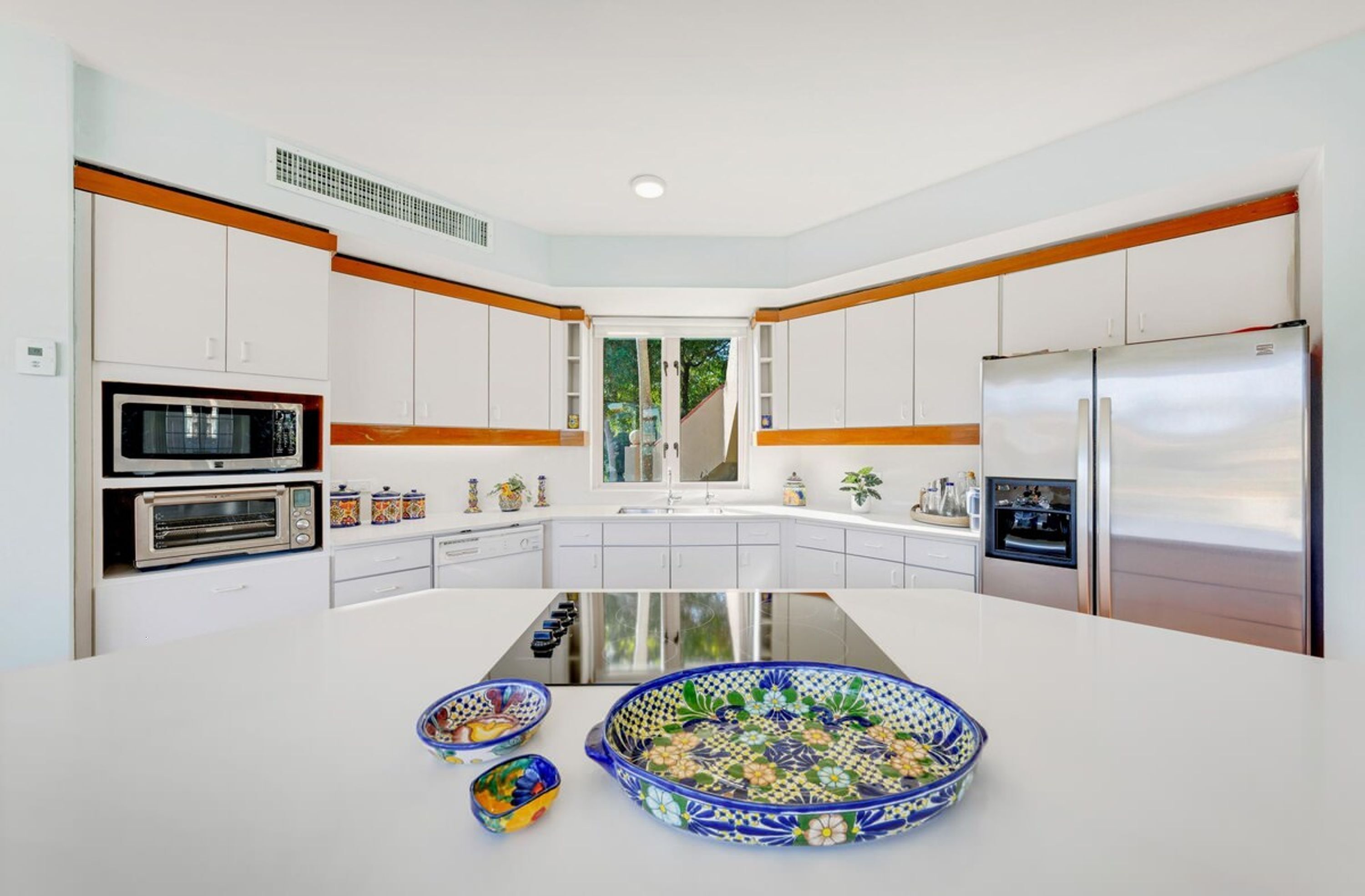 Uma cozinha moderna com armários brancos, eletrodomésticos de aço inoxidável e uma ilha central adornada com tigelas decorativas.