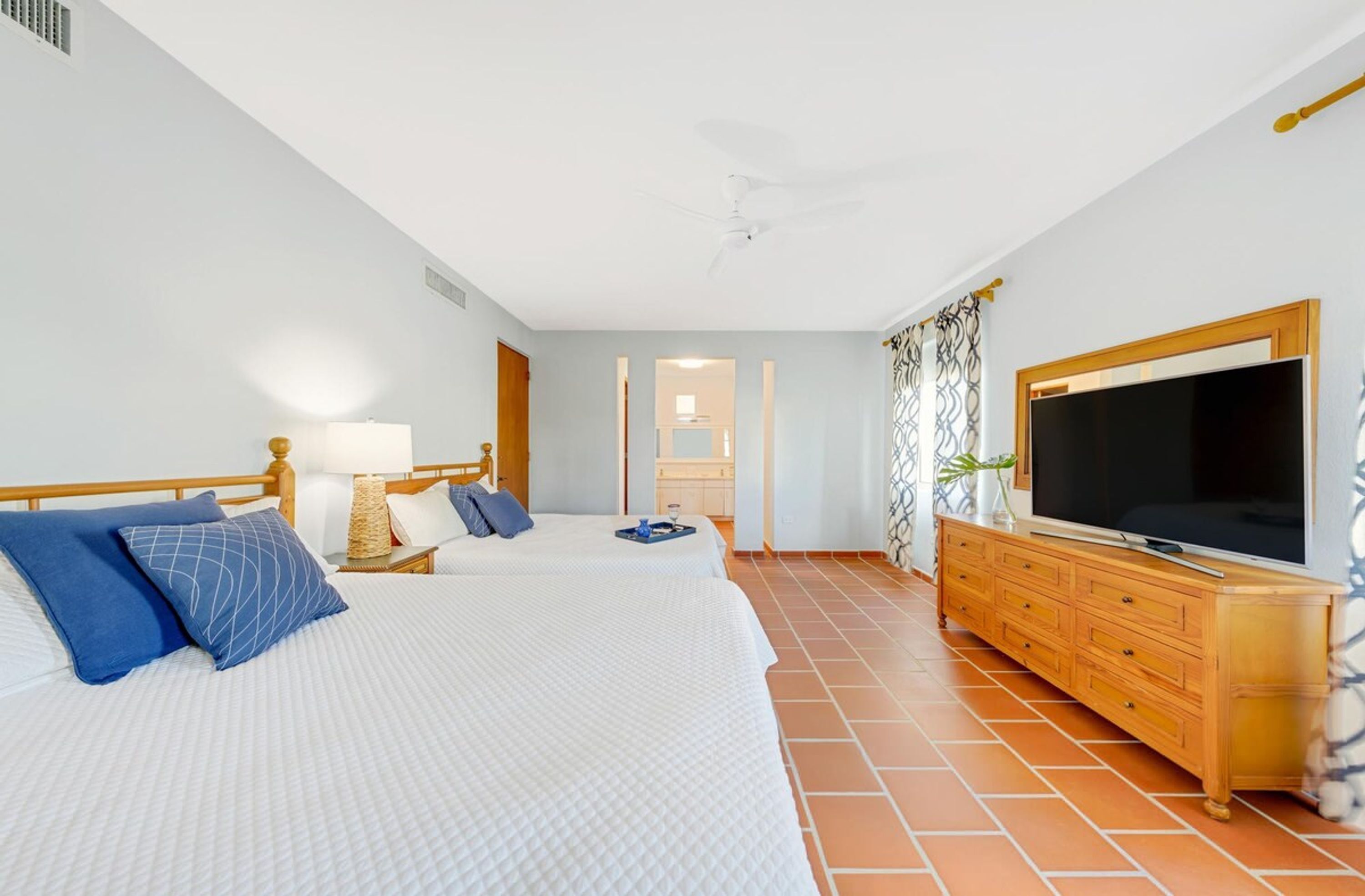 A hotel room with two beds, a TV, a wooden dresser, and a bathroom visible through an open door.
