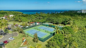 A tennis court surrounded by lush greenery and a view of the ocean. - Villa Quenepa at Lakeside Villas (Vega Alta)