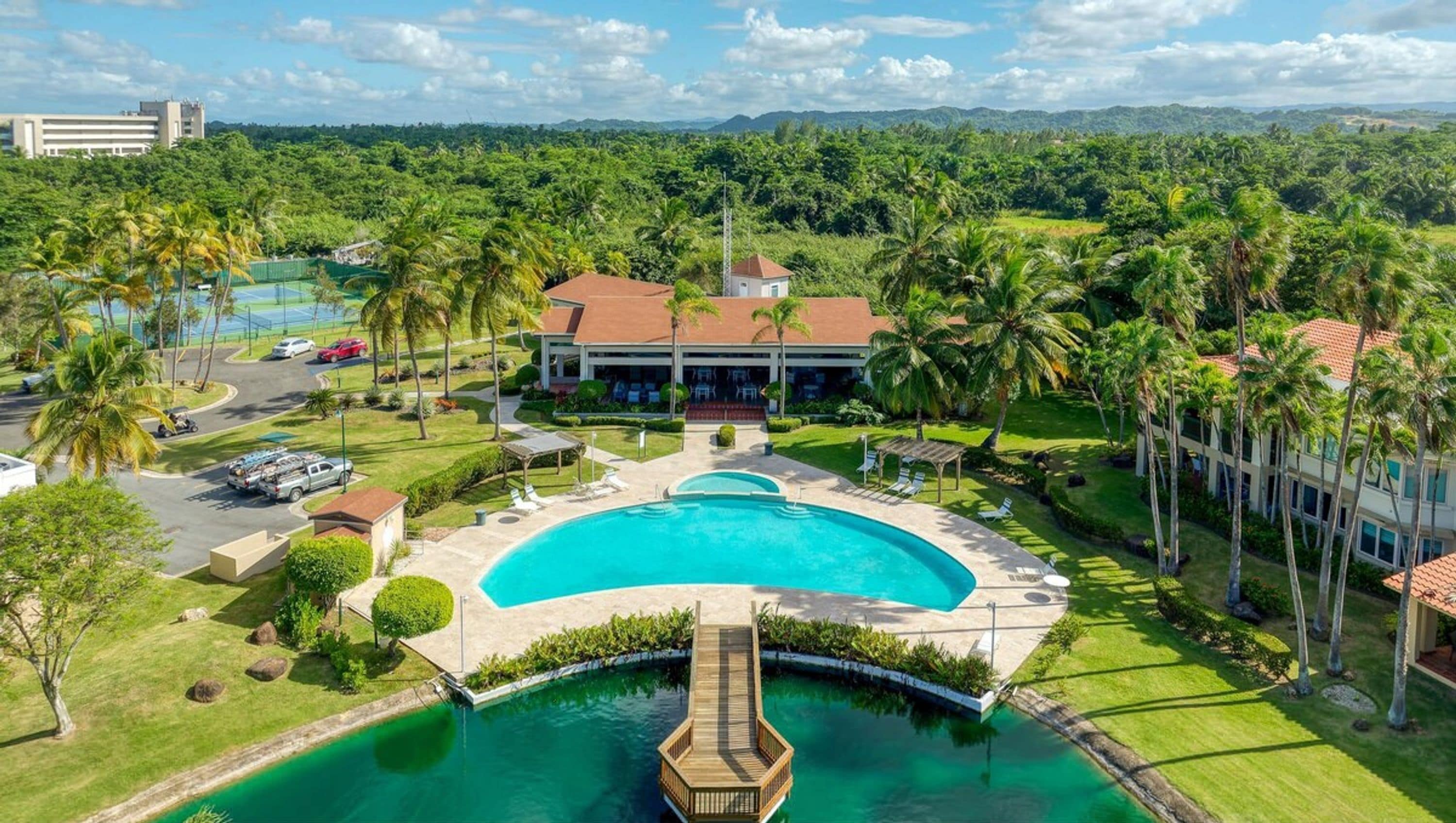 A resort with a large central pool, palm trees, and a view of distant mountains.