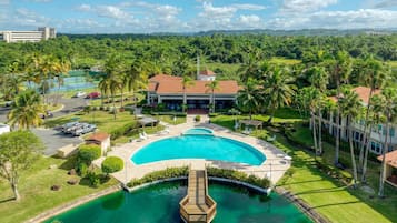 A resort with a large central pool, palm trees, and a view of distant mountains.