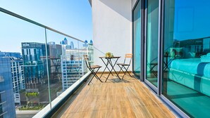 A balcony with a wooden floor, a small table with chairs, and a bed with a blue cover. - Luxurious Studio With Bay View in Sol Bay (Dubai)