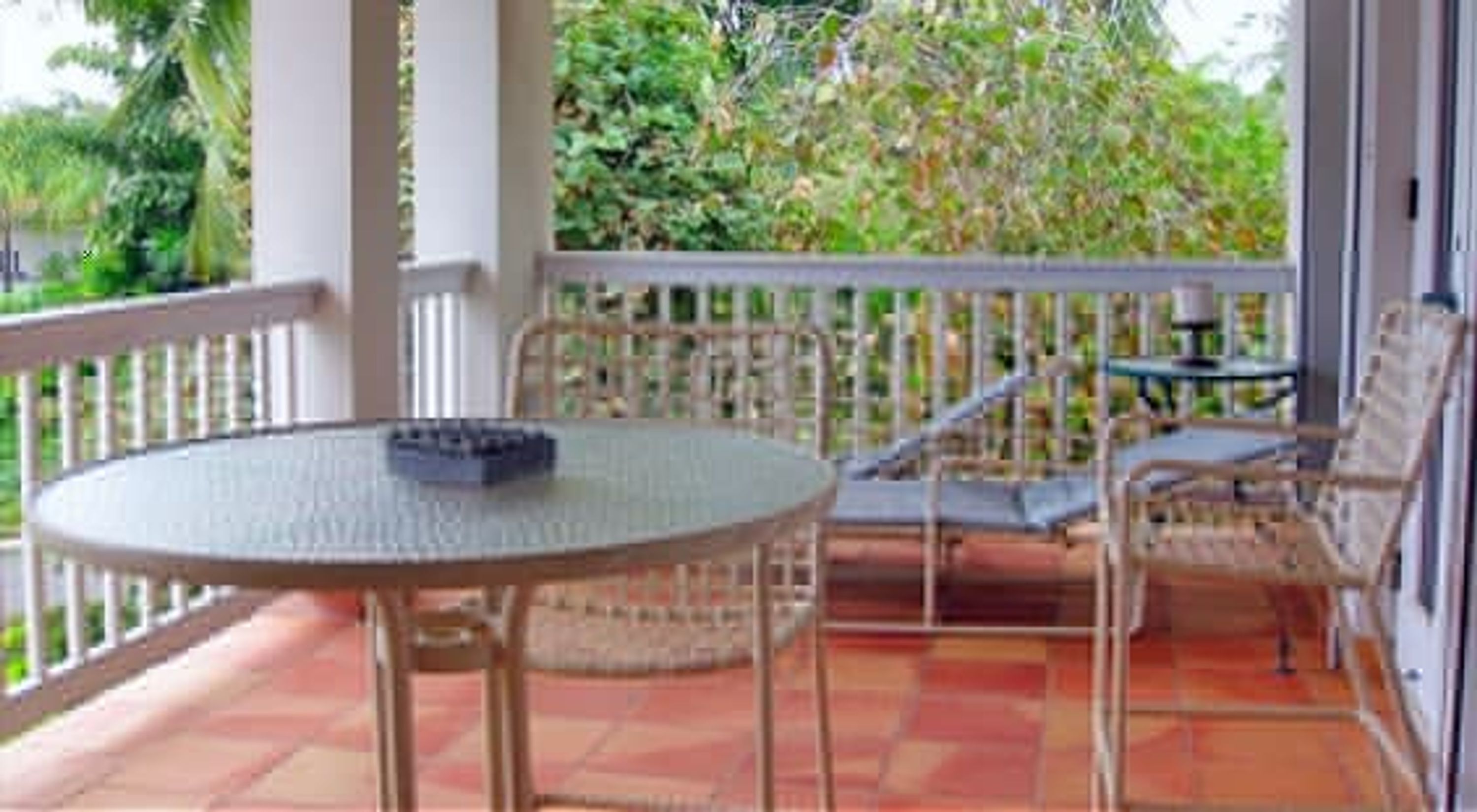 A covered outdoor seating area with a round table and chairs, surrounded by a white railing, overlooking a garden.