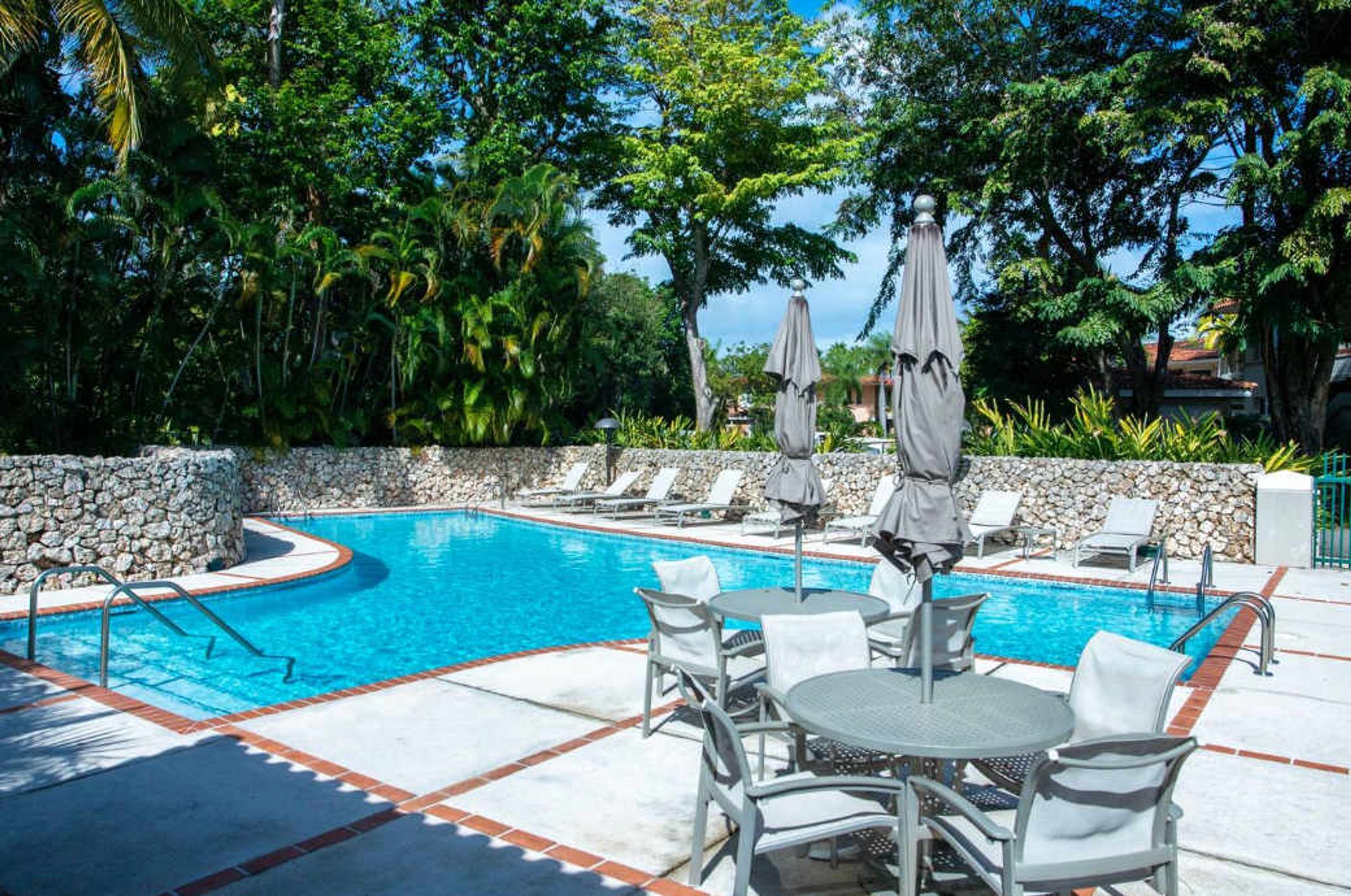 Una piscina con sillas de descanso y sombrillas, rodeada de muros de piedra y vegetación tropical.