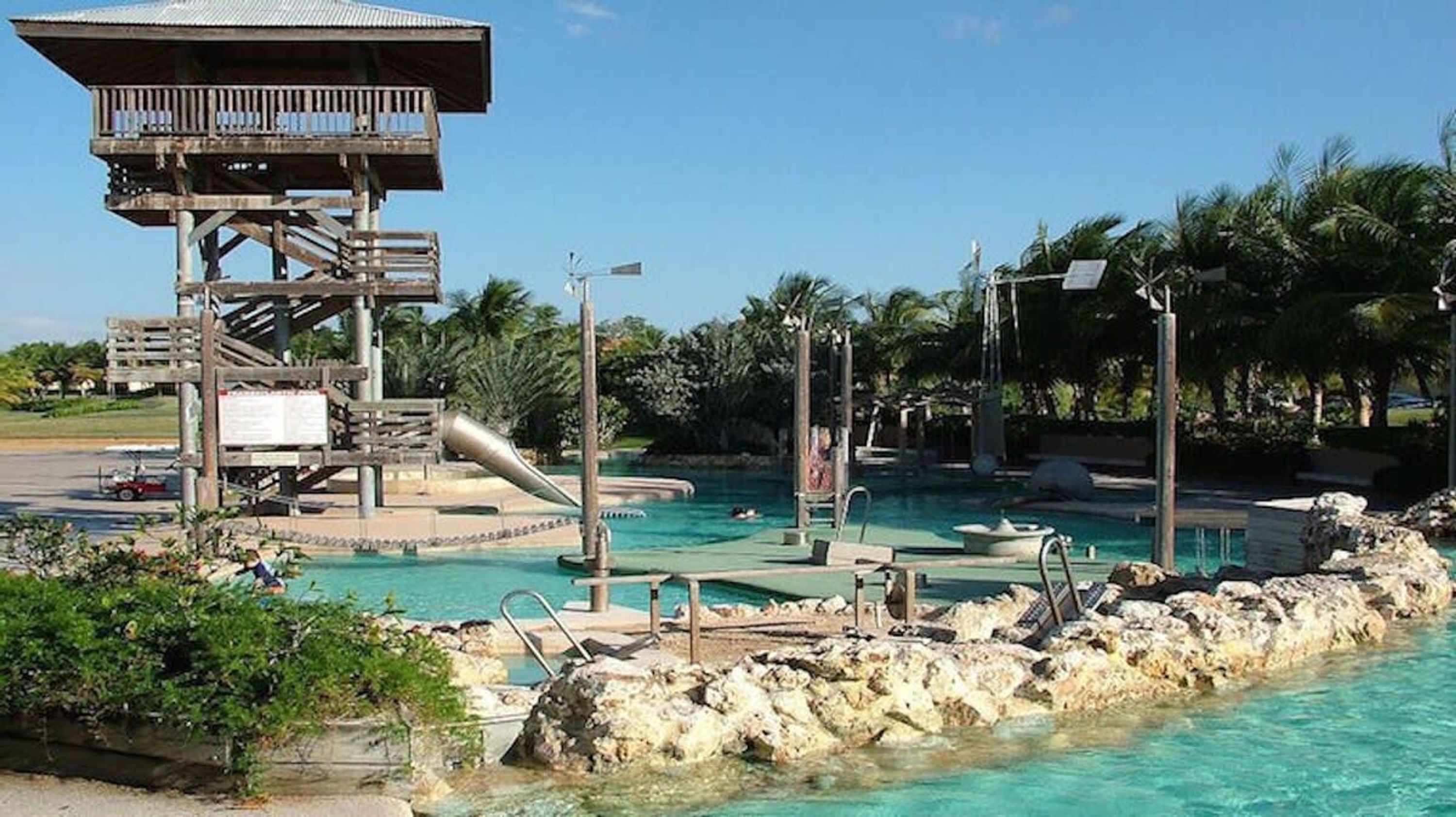 Ein Poolbereich eines Resorts mit Rettungsschwimmturm, mehreren Pools und Palmen.