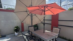 An outdoor patio with a wooden table and chairs, a beige umbrella, and a potted plant. - Senior Suite 3 Bedroom (Georgetown)