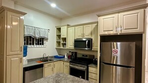 A kitchen with beige cabinets, a granite countertop, a stainless steel refrigerator, and a microwave. - Senior Suite 3 Bedroom (Georgetown)