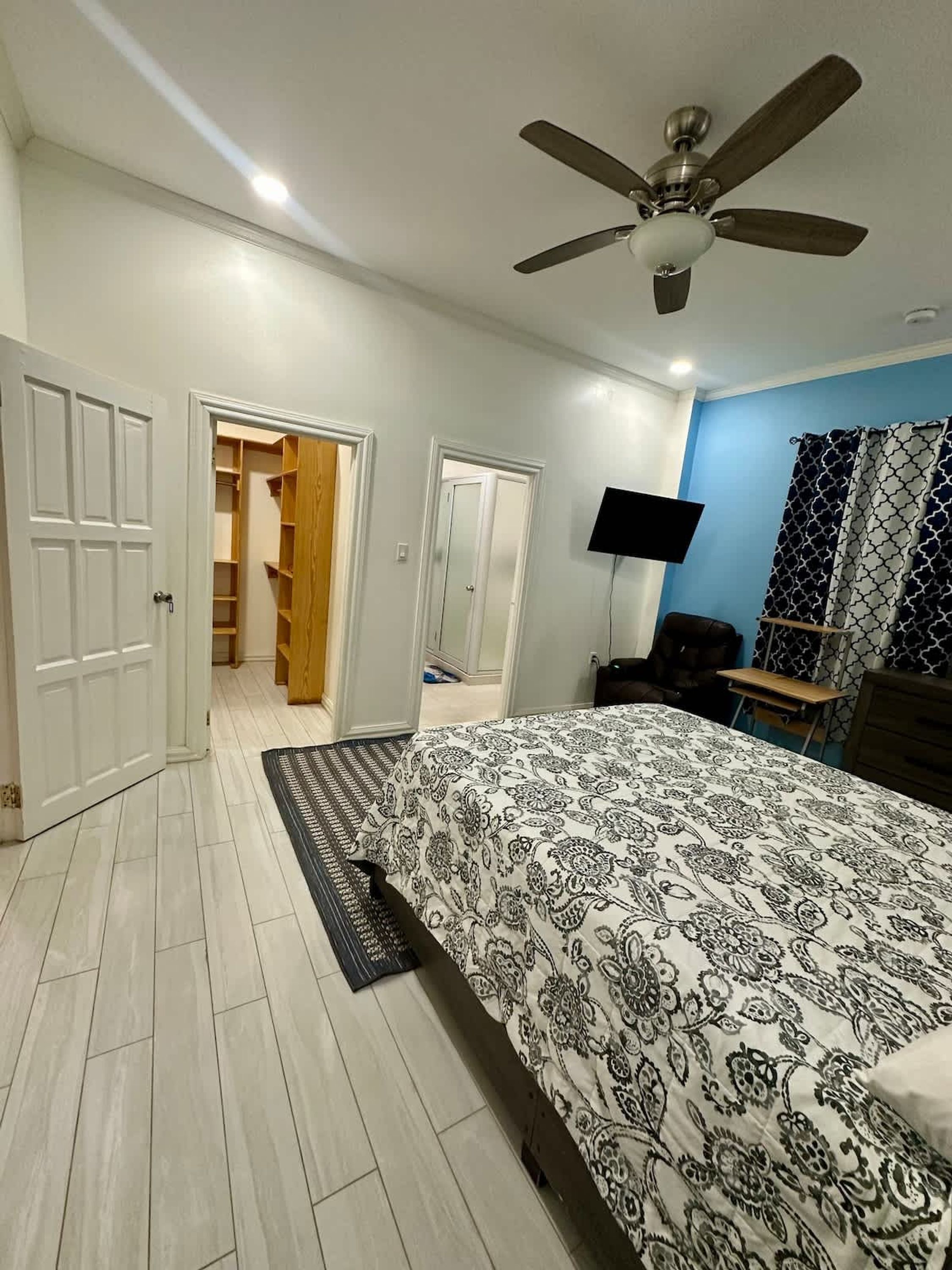 A bedroom with a bed, a ceiling fan, a TV, and a wardrobe.