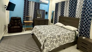 A bedroom with a bed, a ceiling fan, a TV, a chair, a desk, and patterned curtains. - Senior Suite 3 Bedroom (Georgetown)