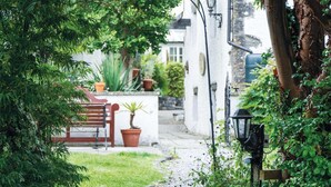 Un étroit sentier de jardin mène à un bâtiment blanc, où se trouvent un banc rouge et des plantes en pot.