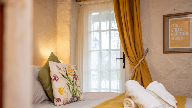 Une chambre d’hôtel avec un lit, une fenêtre avec des rideaux, une citation encadrée au mur et un coussin décoratif.