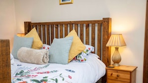 Una cama bien hecha con ropa de cama floral, un cabecero de madera y una lámpara de noche.