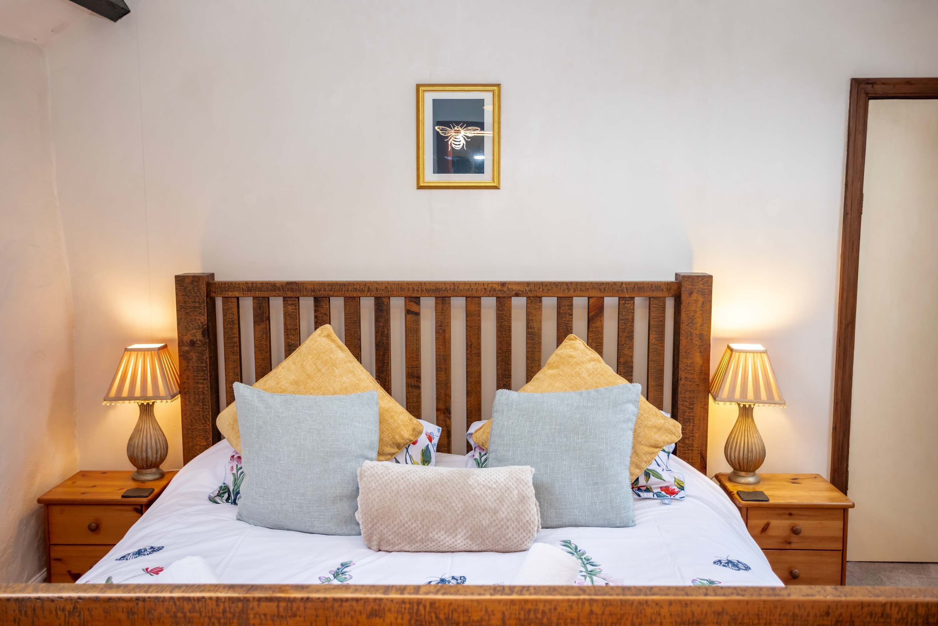 A neatly made bed with a wooden headboard, two bedside tables with lamps, and a framed picture on the wall.