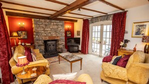 A cozy living room with a stone fireplace, comfortable sofas, a television, and a large window with curtains. - Hall House 3 Bedroom House St Florence (Tenby)