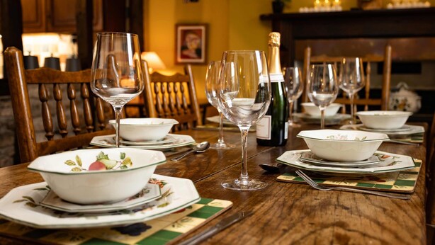 A dining table set with white plates, bowls, and wine glasses, with a bottle of champagne and candles on the table. - Hall House 3 Bedroom House St Florence (Tenby)