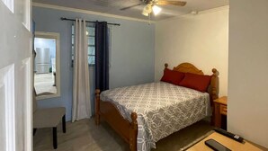 A bedroom with a bed, a ceiling fan, a nightstand, a chair, a window with curtains, and a door. - Junior Suite in Pigeon Island (Georgetown)