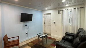 A living room with a flat-screen TV, a sofa, a wooden chair, and a glass coffee table. - Junior Suite in Pigeon Island (Georgetown)