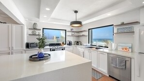 A modern kitchen with white cabinetry, a central island, and a large window offering a view of the sea. - 4 BR Kikita Beach Villa Oceanfront w Pool (Dorado)