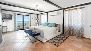 A bedroom with a bed, a bedside table, a chair, a TV, and a view of the sea. - 4 BR Kikita Beach Villa Oceanfront w Pool (Dorado)
