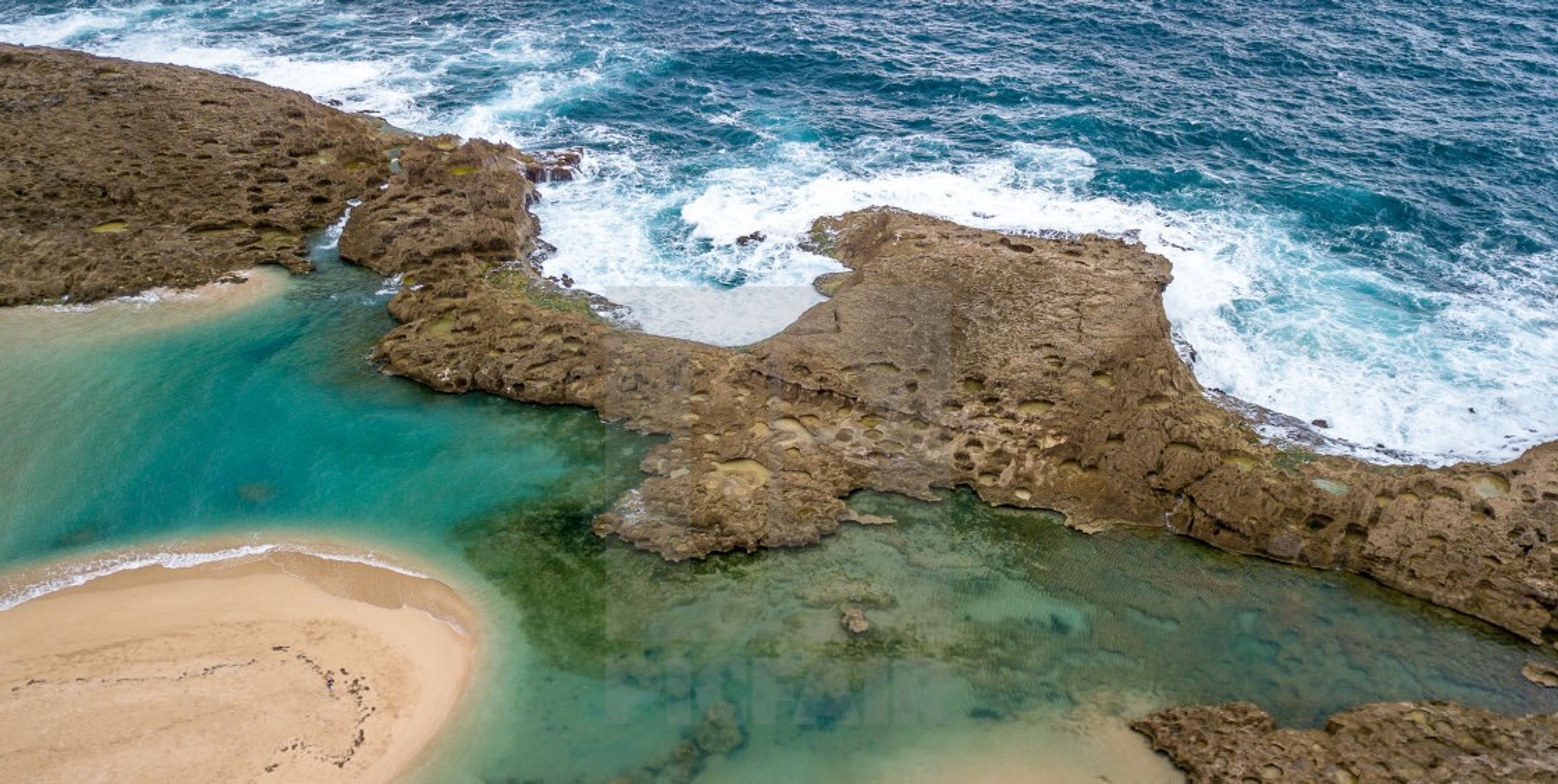 Un paisaje costero con formaciones rocosas, aguas turquesas cristalinas y una playa arenosa.